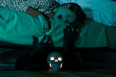 Photo of Childhood phobia. Scared girl looking at monster under bed indoors