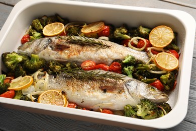 Photo of Delicious fish with vegetables and lemon in baking dish on table