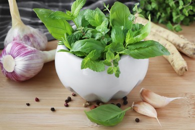 Photo of Mortar with different fresh herbs near garlic, horseradish roots and black peppercorns on wooden table, closeup