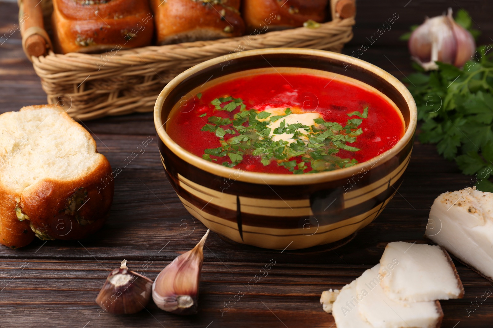 Photo of Delicious borsch served with pampushky and salo on wooden table. Traditional Ukrainian cuisine