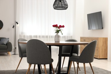 Photo of Chairs and table with vase of red rose flowers in dining room. Stylish interior