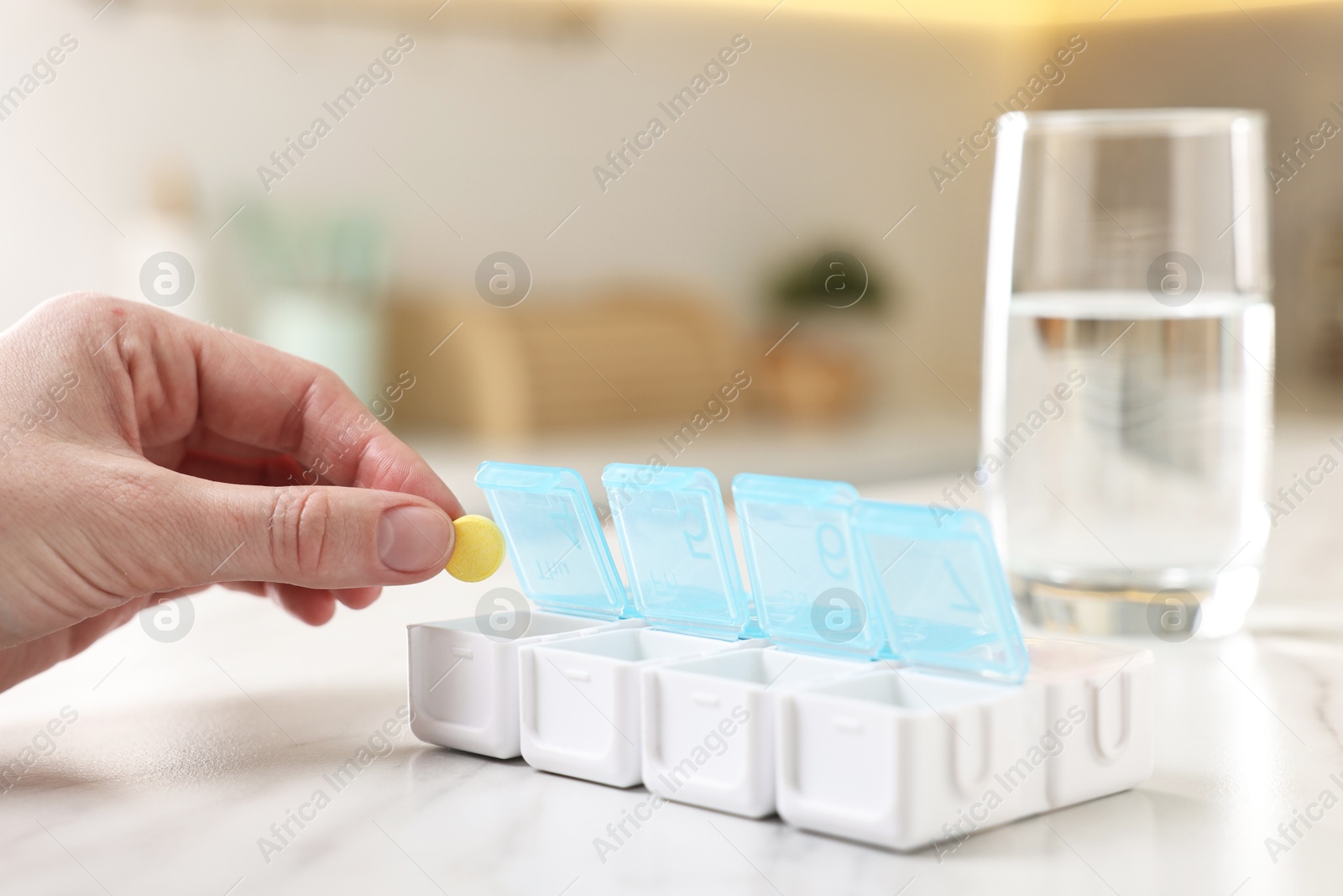 Photo of Woman with pills, organizer and glass of water at white marble table, closeup