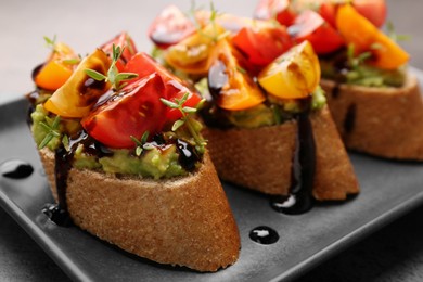 Photo of Delicious bruschettas with avocado, tomatoes and balsamic vinegar on gray plate, closeup