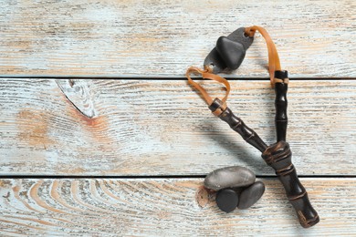 Photo of Black slingshot with stones on old light blue wooden table, flat lay. Space for text