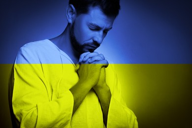 Image of Pray for Ukraine. Double exposure of man praying and Ukrainian national flag