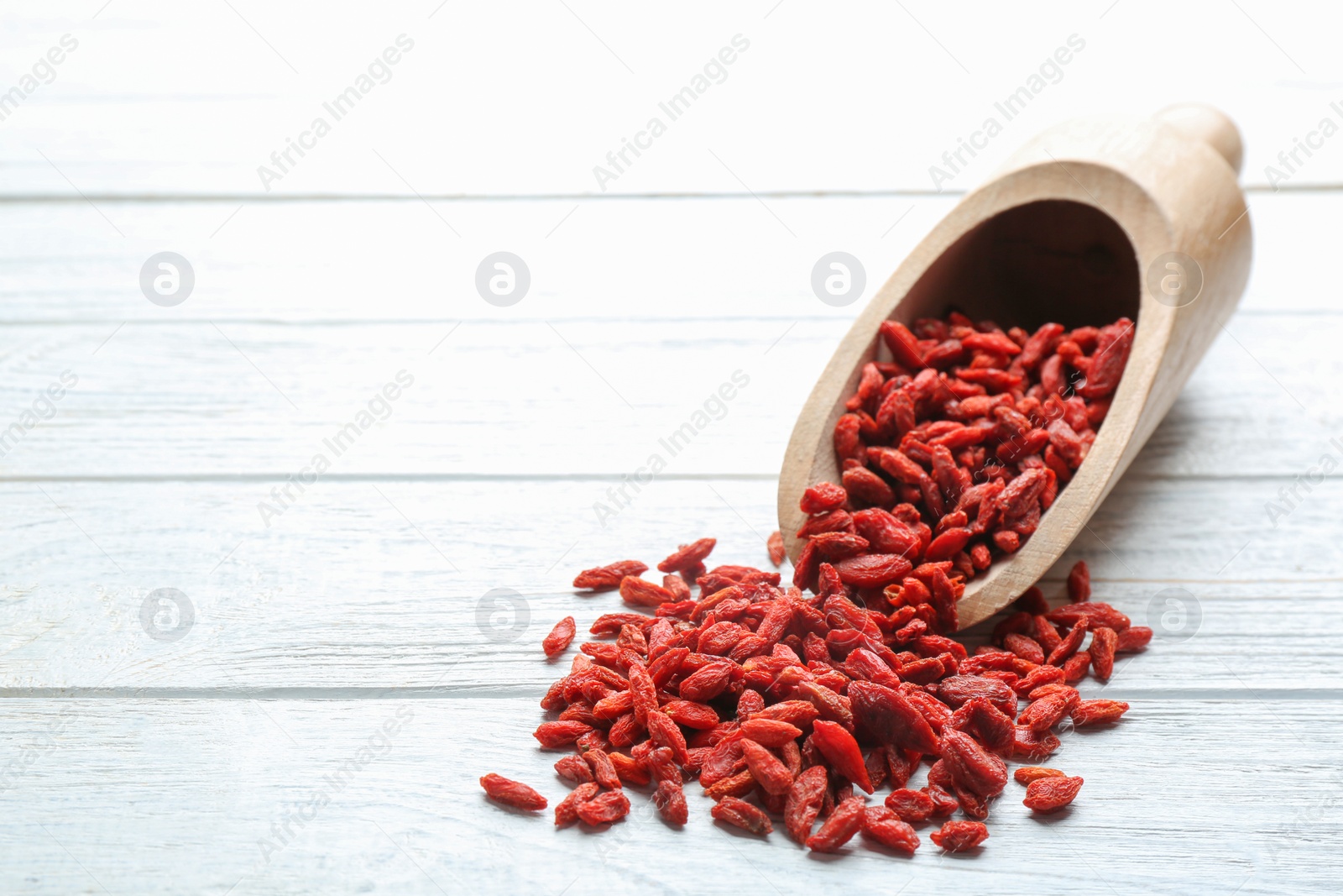 Photo of Scoop and dried goji berries on white wooden table, space for text. Healthy superfood