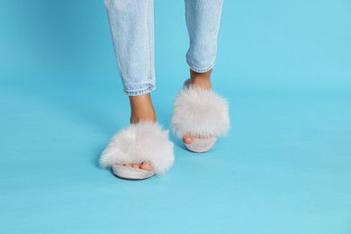 Woman in fluffy slippers on light blue background, closeup