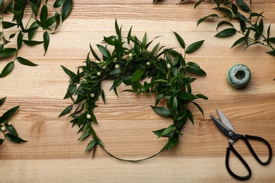 Photo of Unfinished mistletoe wreath and florist supplies on wooden table, flat lay. Traditional Christmas decor