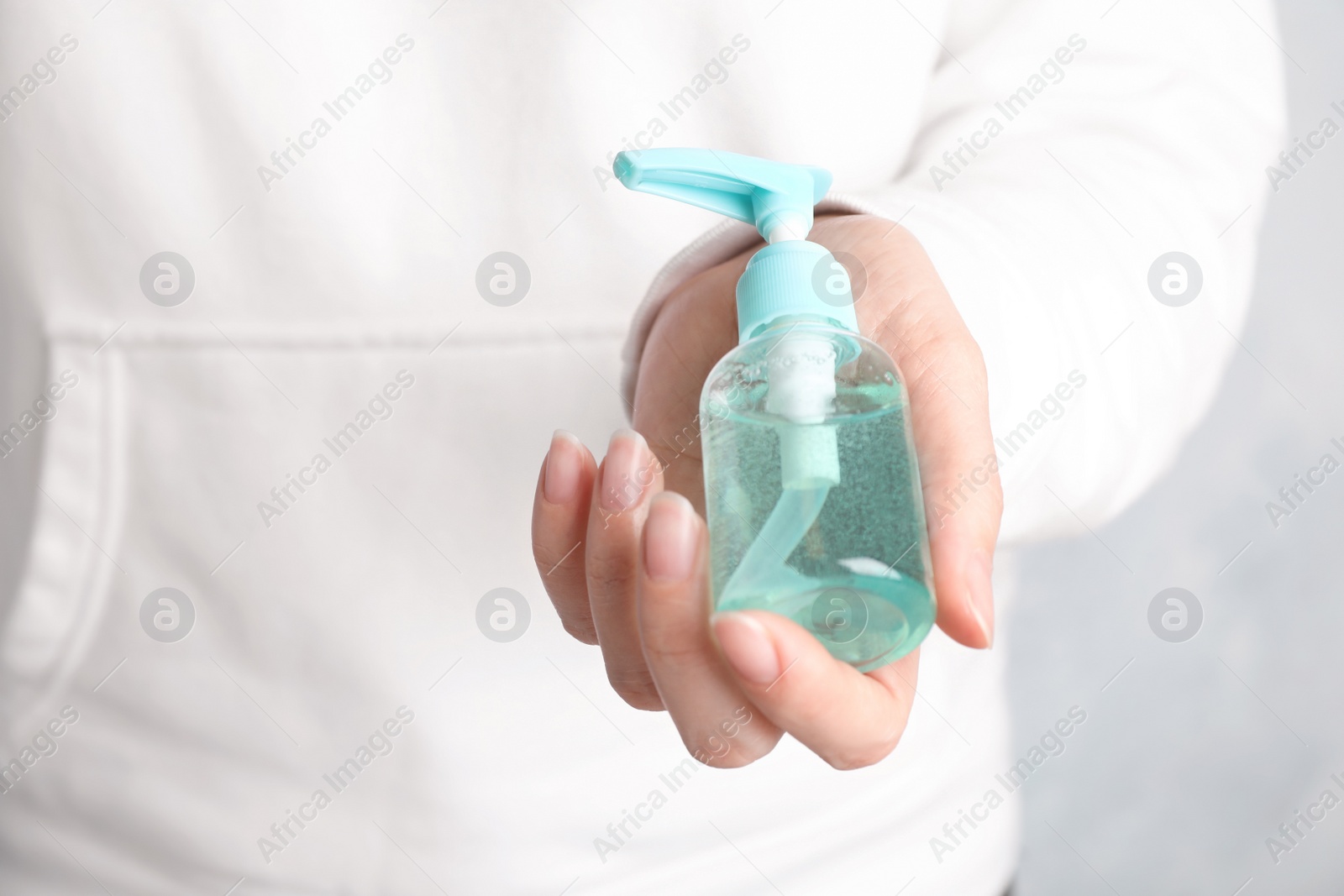 Photo of Woman holding antiseptic gel on light background, closeup