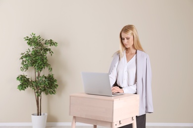 Photo of Young woman using laptop at stand up workplace against light wall