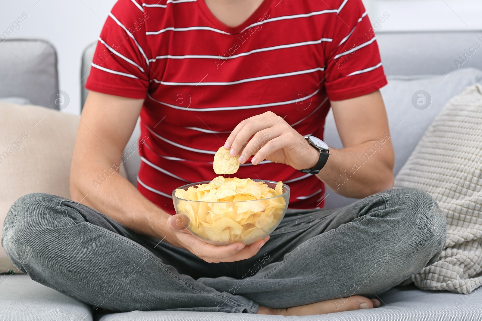 Photo of Man with bowl of potato chips sitting on sofa, closeup