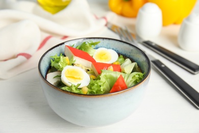 Delicious salad with crab sticks and eggs in bowl on white table