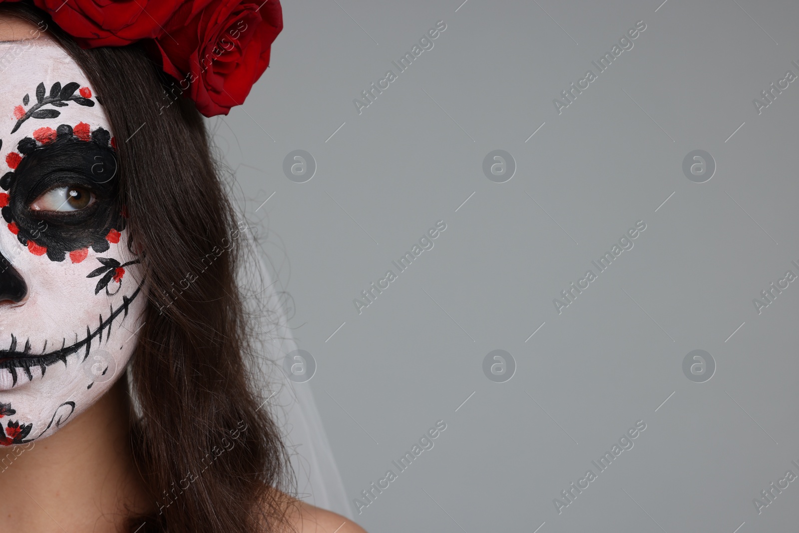 Photo of Young woman in scary bride costume with sugar skull makeup and flower crown on light grey background, closeup and space for text. Halloween celebration