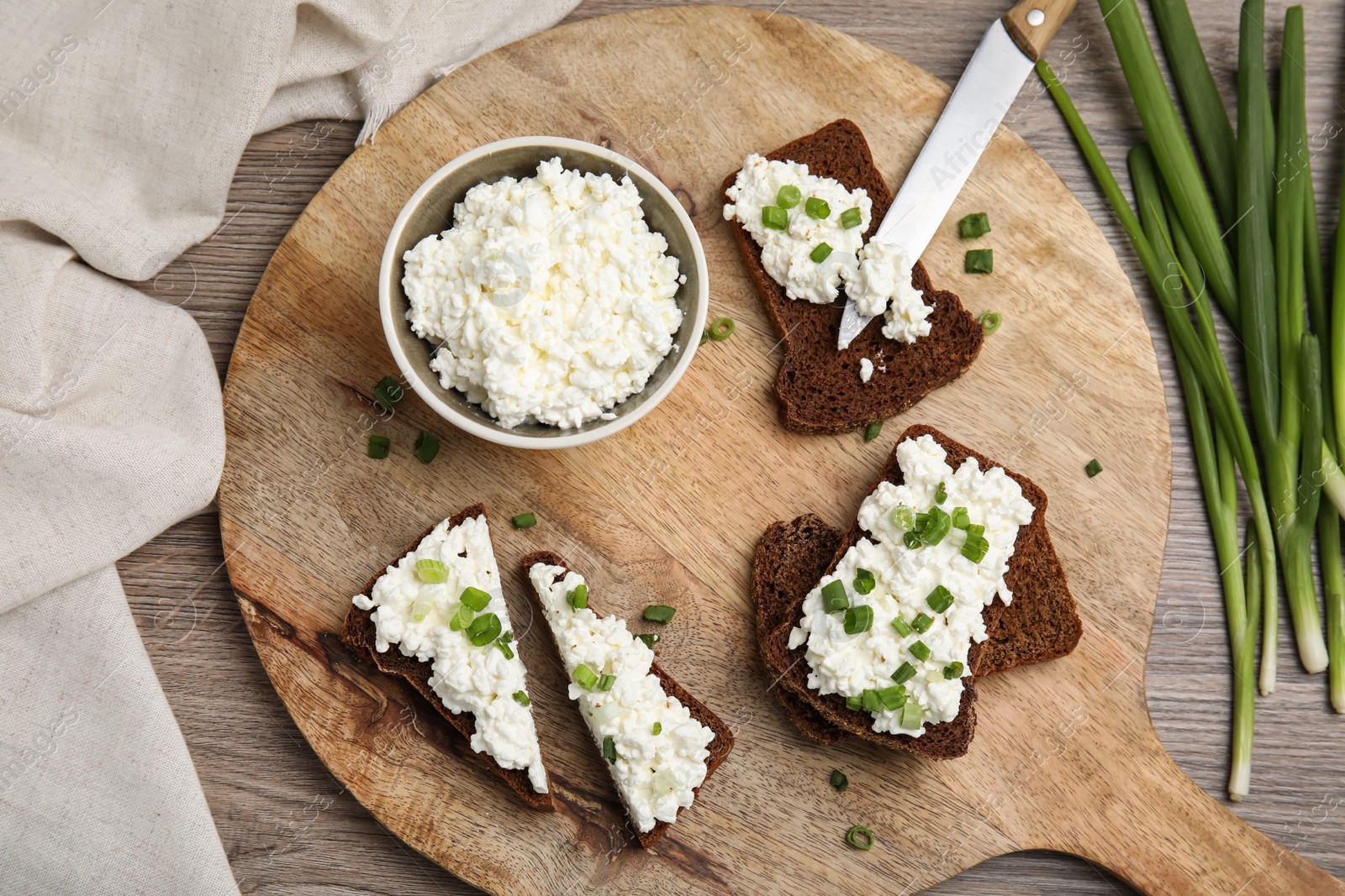 Photo of Bread with cottage cheese and green onion on wooden table, flat lay