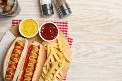 Delicious hot dogs with mustard, ketchup and potato fries on white wooden table, flat lay. Space for text