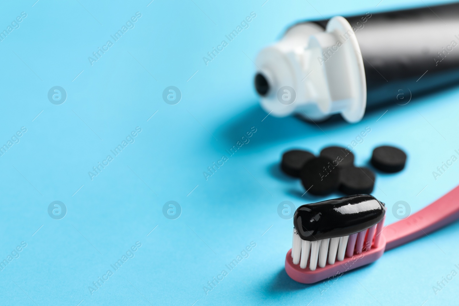 Photo of Brush with charcoal toothpaste on light blue background. Space for text