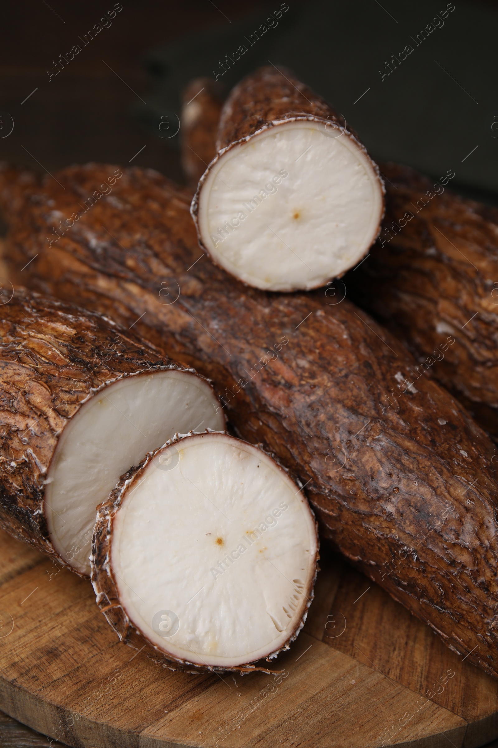 Photo of Whole and cut cassava roots on wooden table, closeup