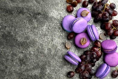 Photo of Delicious macarons and grapes on grey table, flat lay. Space for text