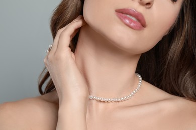 Photo of Young woman wearing elegant pearl jewelry on grey background, closeup