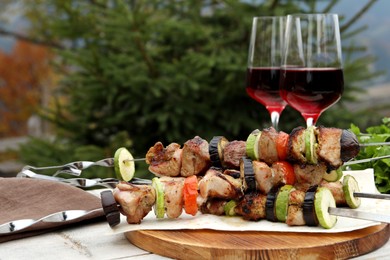 Photo of Metal skewers with delicious meat, vegetables and wine served on wooden table outdoors