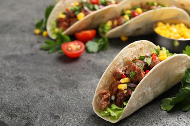 Photo of Delicious tacos with meat and vegetables on gray textured table, closeup. Space for text