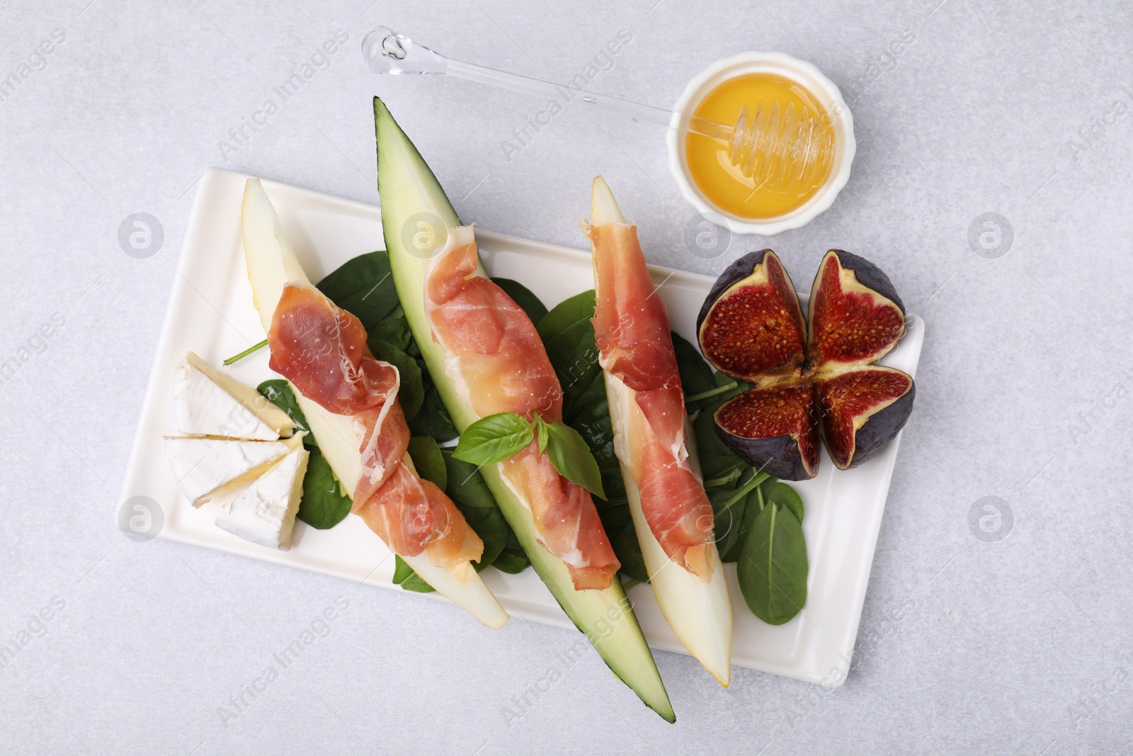 Photo of Tasty melon, jamon and figs served on light grey table, flat lay