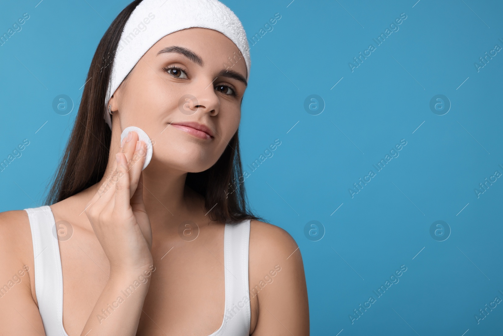 Photo of Young woman with cotton pad on light blue background. Space for text