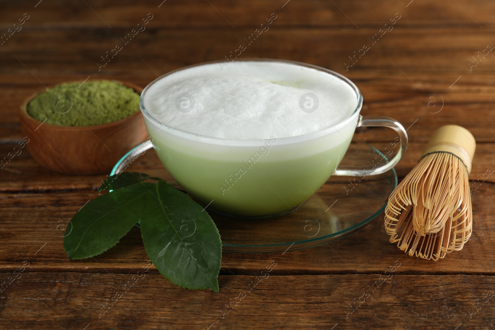 Photo of Cup of fresh matcha latte, bamboo whisk and green leaves on wooden table, closeup
