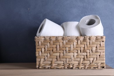 Photo of Toilet paper rolls in wicker basket on wooden table near blue wall