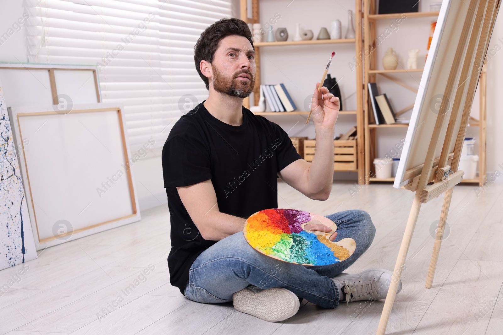 Photo of Man painting in studio. Using easel to hold canvas