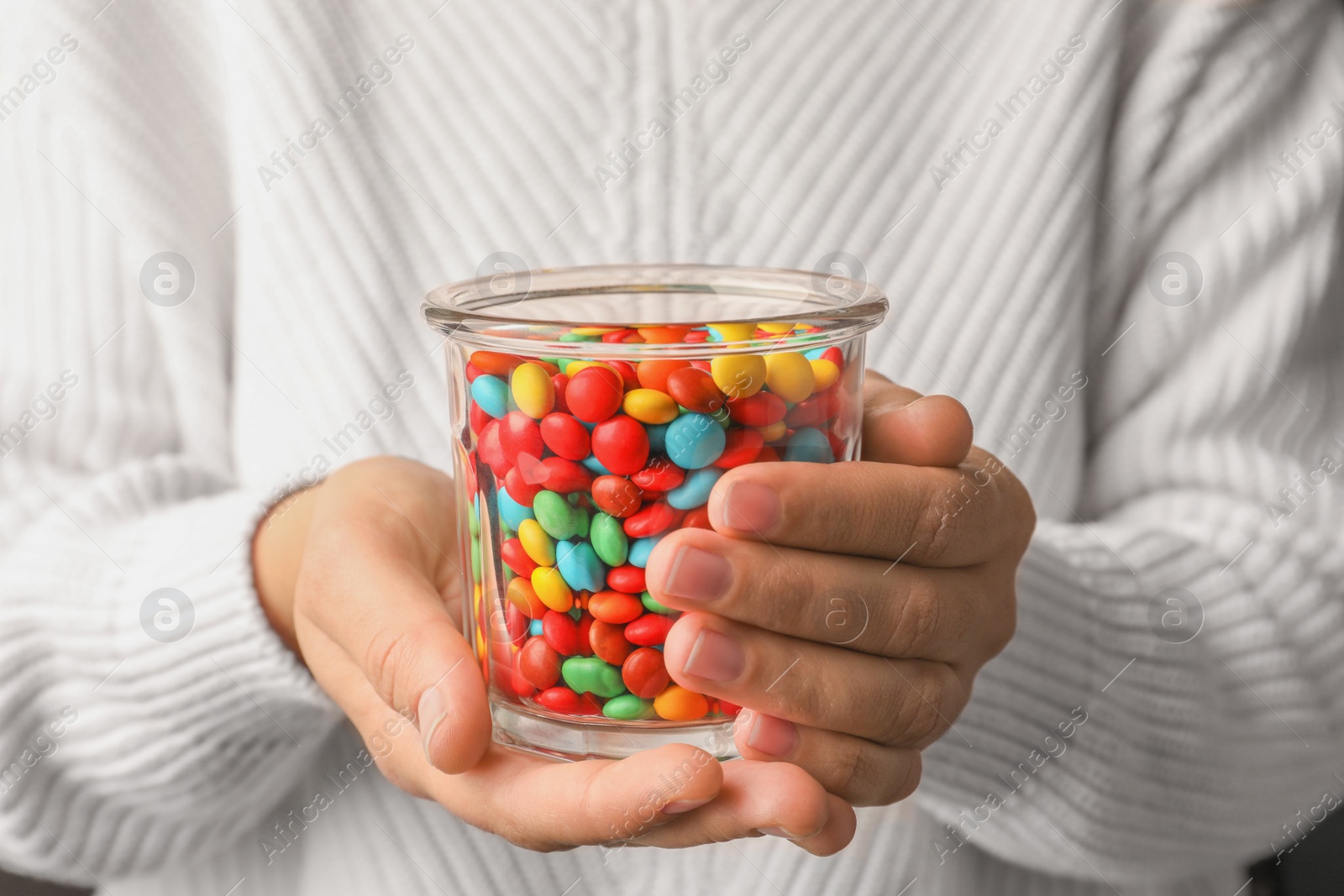 Photo of Woman with glass of tasty colorful candies, closeup