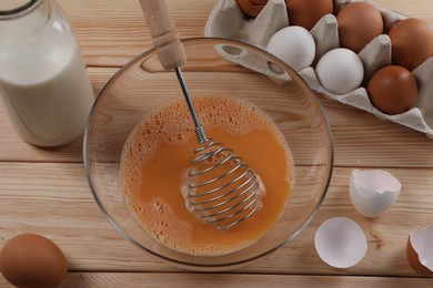 Making dough. Beaten eggs in bowl, shells and milk on wooden table, flat lay