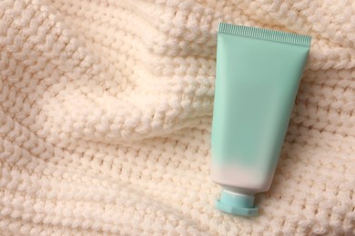 Photo of Winter skin care. Hand cream on white knitted cloth, top view. Space for text