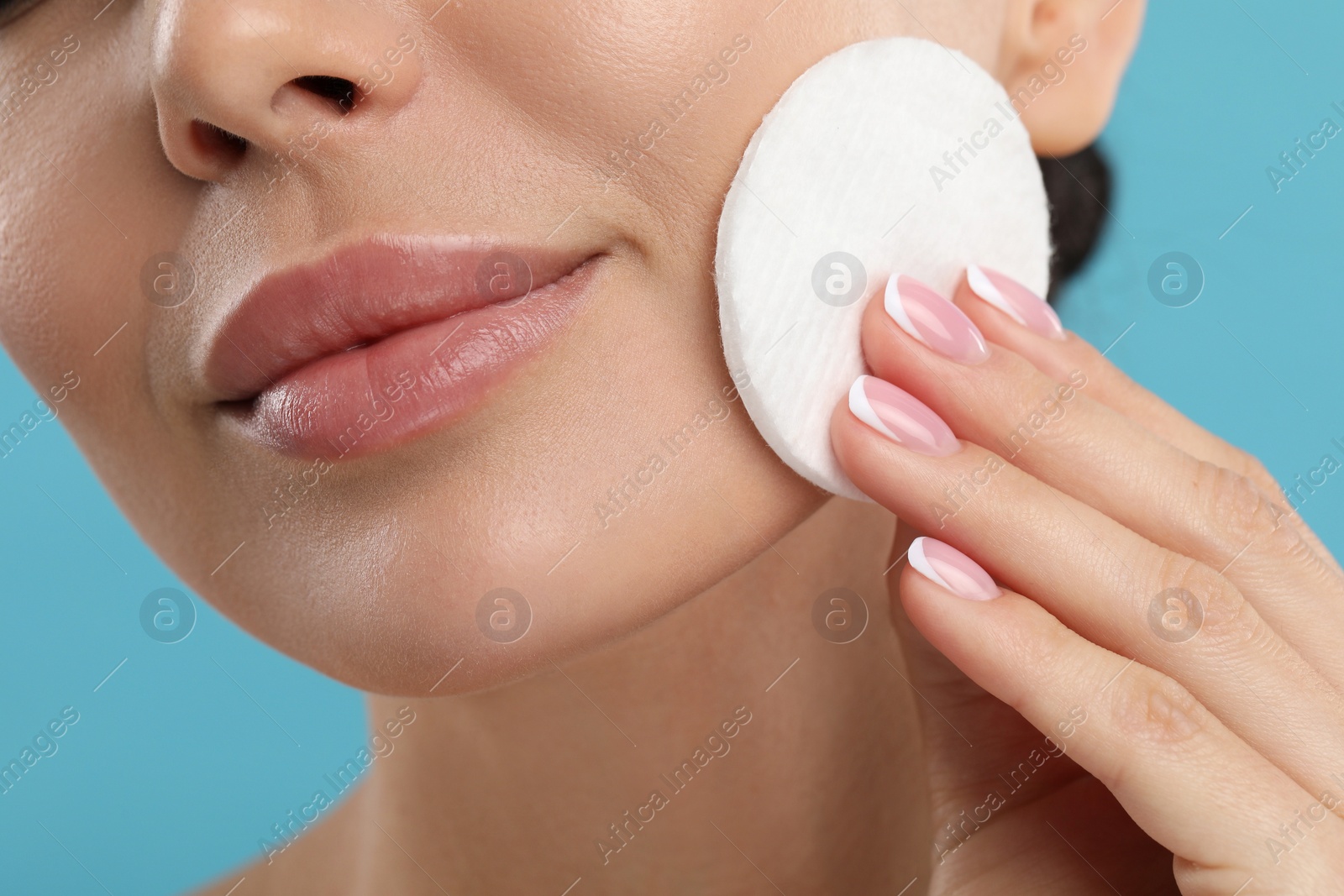 Photo of Beautiful woman removing makeup with cotton pad on light blue background, closeup