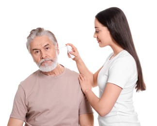 Young woman spraying medication into man's ear on white background