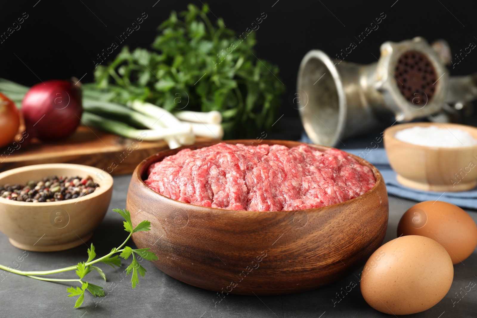 Photo of Raw ground meat in bowl and different products on grey table