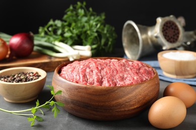 Raw ground meat in bowl and different products on grey table