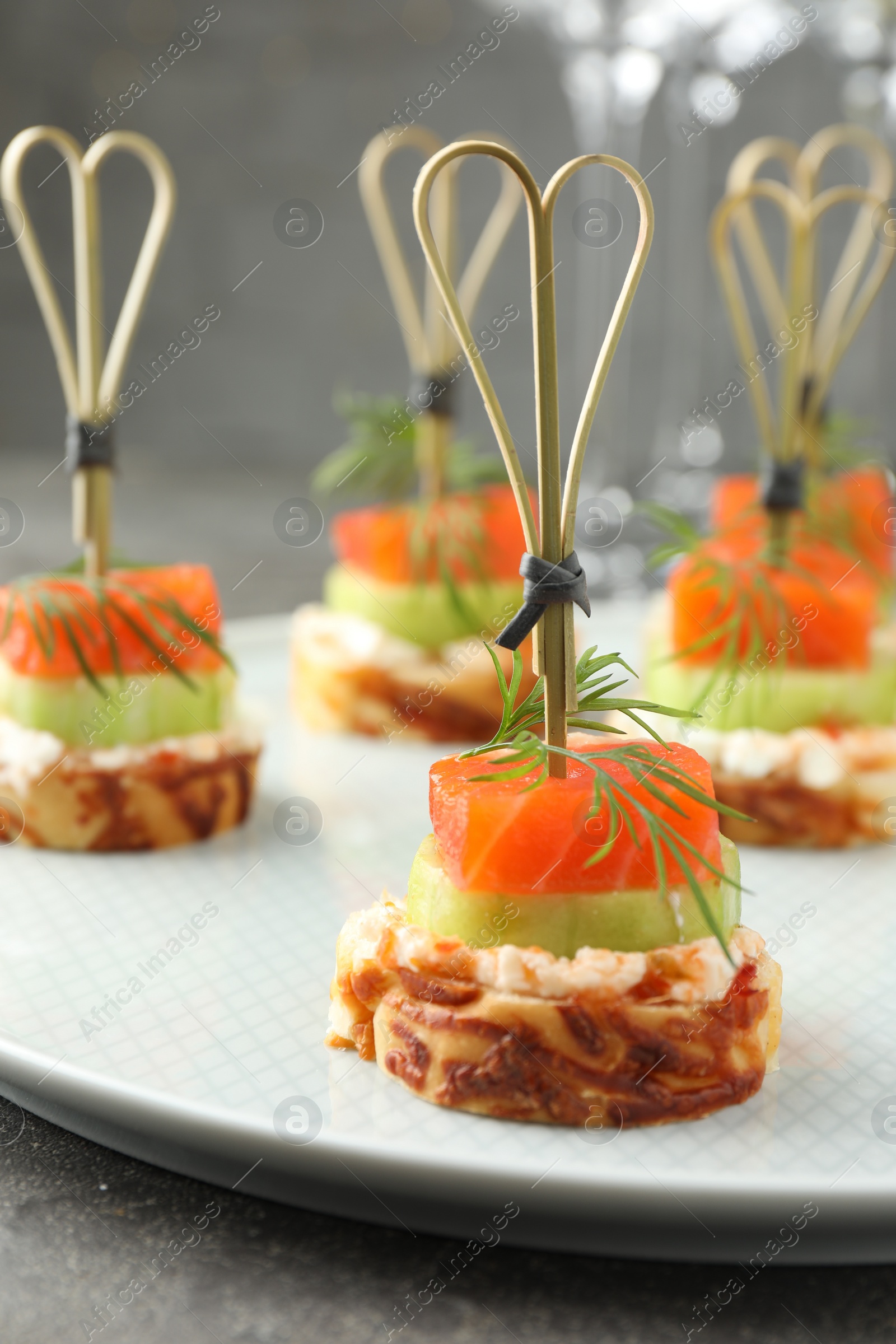 Photo of Tasty canapes with salmon, cucumber, bread and cream cheese on grey table, closeup