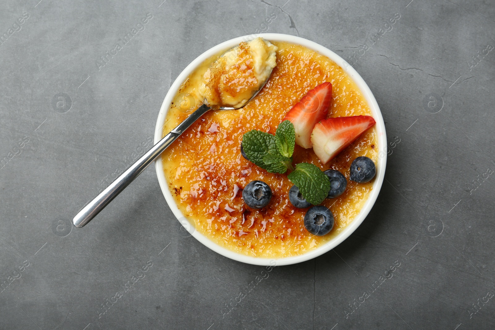 Photo of Delicious creme brulee with berries and mint in bowl on grey table, top view