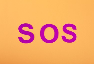 Photo of Abbreviation SOS made of paper letters on orange background, top view