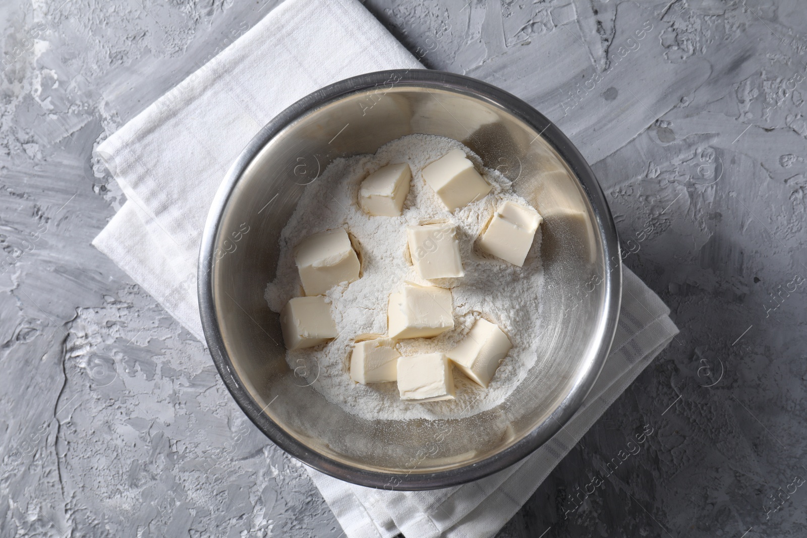 Photo of Making shortcrust pastry. Flour and butter in bowl on grey table, top view