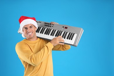 Photo of Man in Santa hat playing synthesizer on light blue background. Christmas music