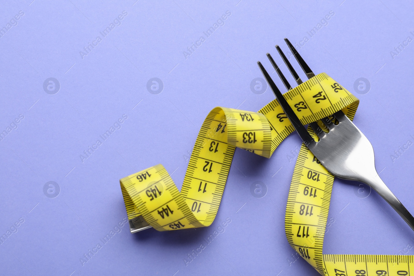 Photo of Fork with measuring tape on purple background, top view with space for text. Diet concept