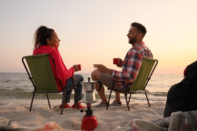 Photo of Couple resting in camping chairs near sea at sunset