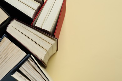 Photo of Many hardcover books on light yellow background, closeup. Space for text