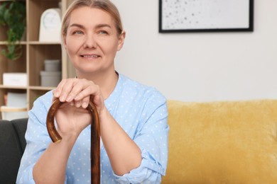 Photo of Senior woman with walking cane sitting on sofa at home. Space for text