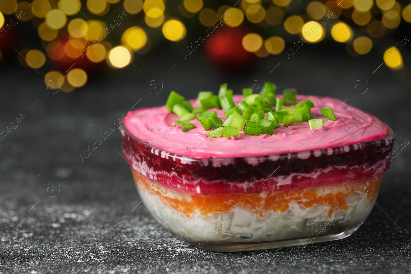 Photo of Herring under fur coat salad on grey table against blurred festive lights, closeup with space for text. Traditional Russian dish