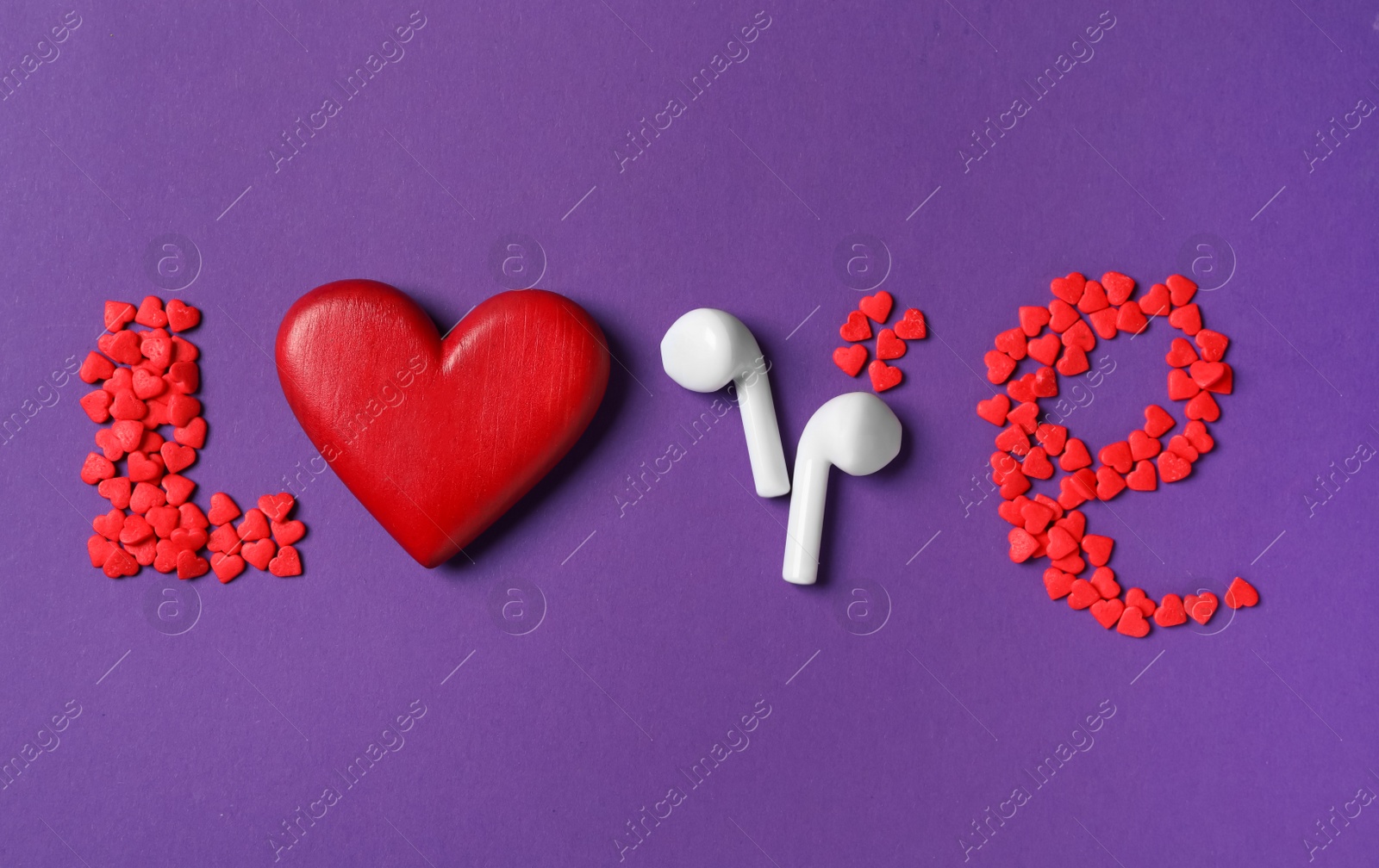 Photo of Word Love made with sprinkles, red heart and modern earphones on purple background, flat lay. Listening music songs