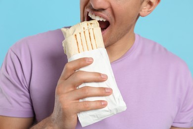 Man eating delicious shawarma on turquoise background, closeup