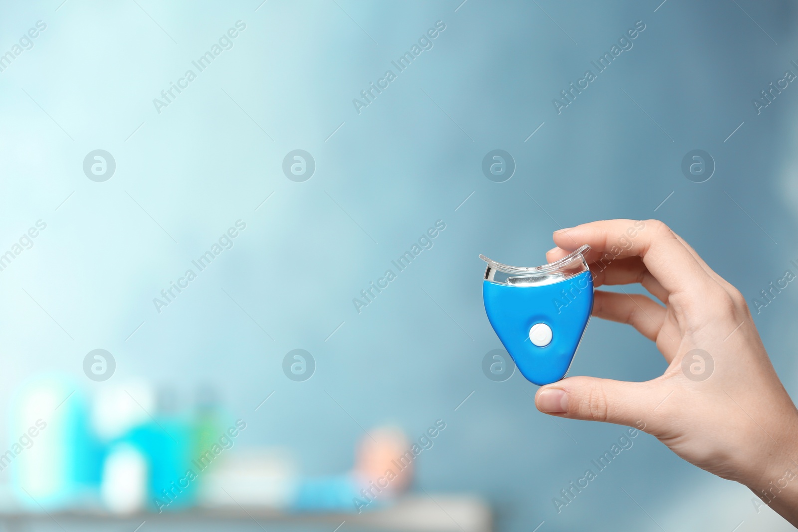 Photo of Woman holding teeth whitening device on blurred background. Space for text